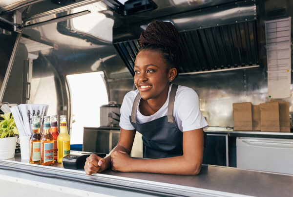 Food Truck Insurance - Smiling Woman in an Apron Leaning Over the Counter and Working in a Food Truck